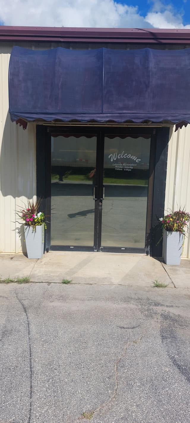 Storefront entrance with blue awning, glass doors, and white planters with flowers