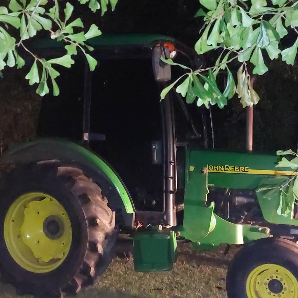 Green John Deere tractor with yellow wheel rims parked at night under tree branches