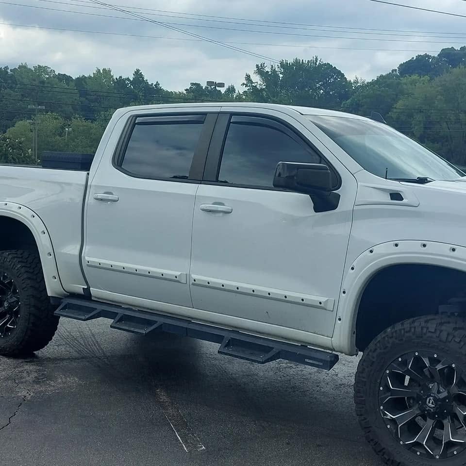 White lifted pickup truck with custom wheels and running boards parked outdoors