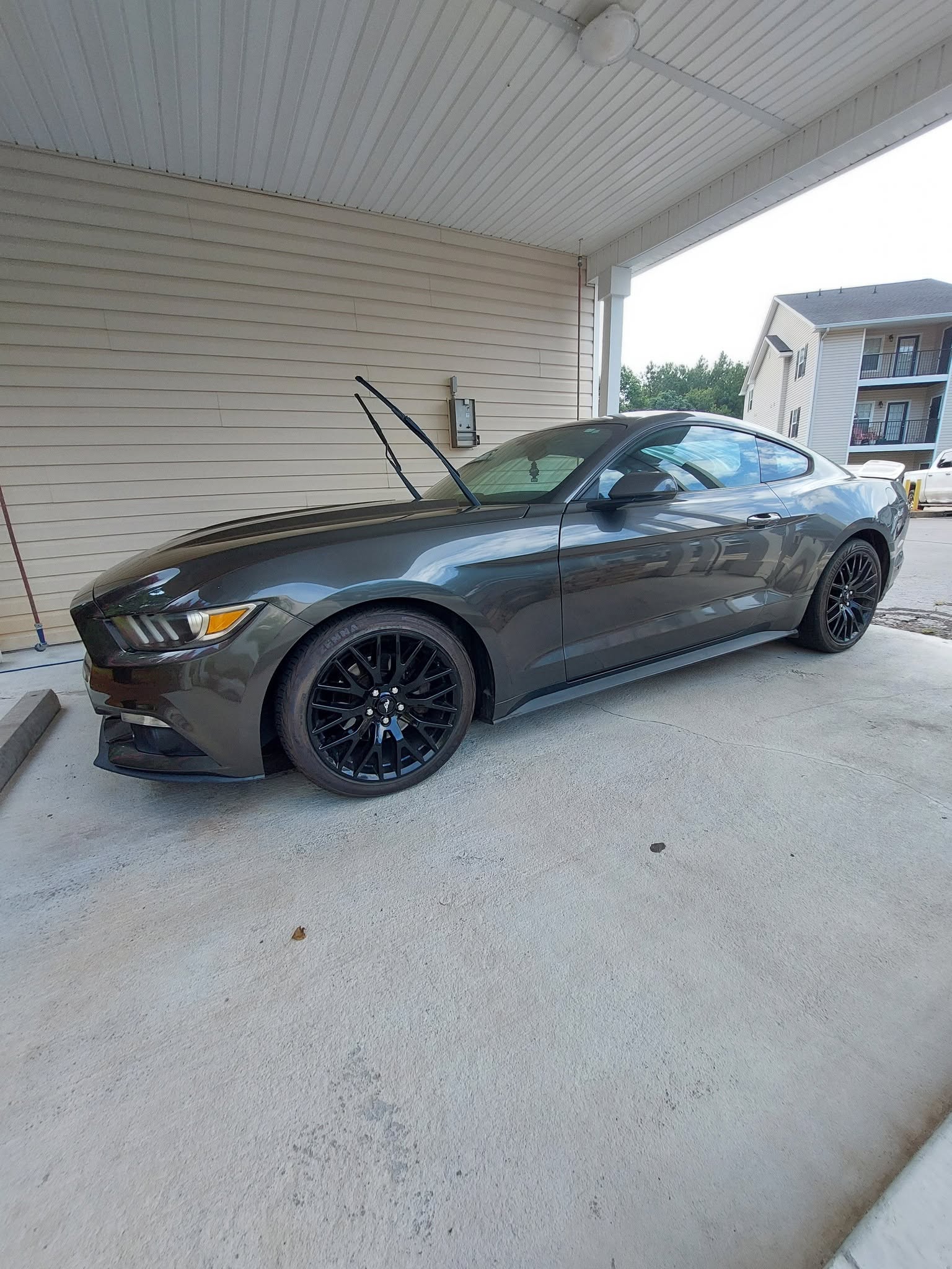 Gray Ford Mustang with open hood parked under carport
