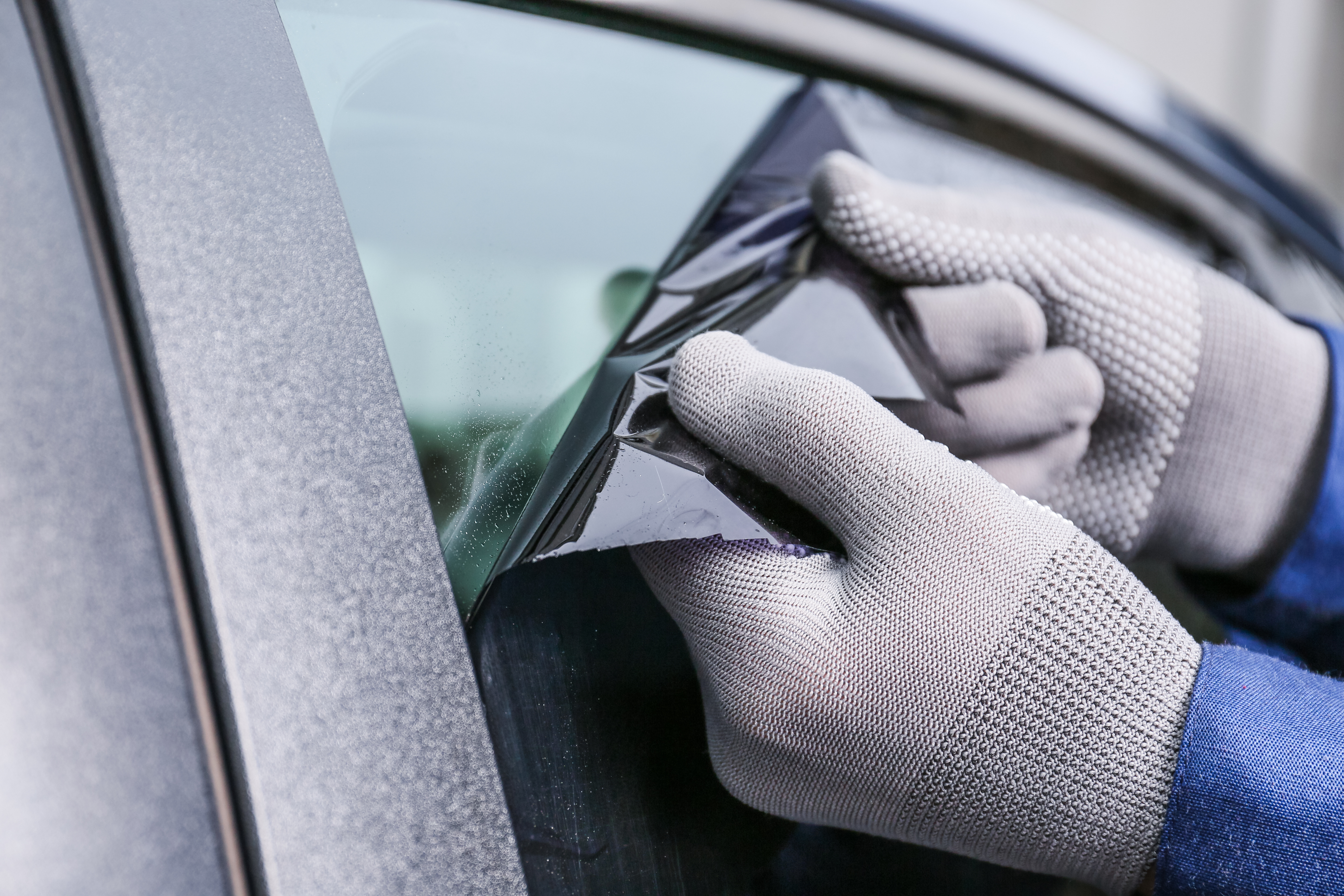 Gloved hand removing car window tint with squeegee tool